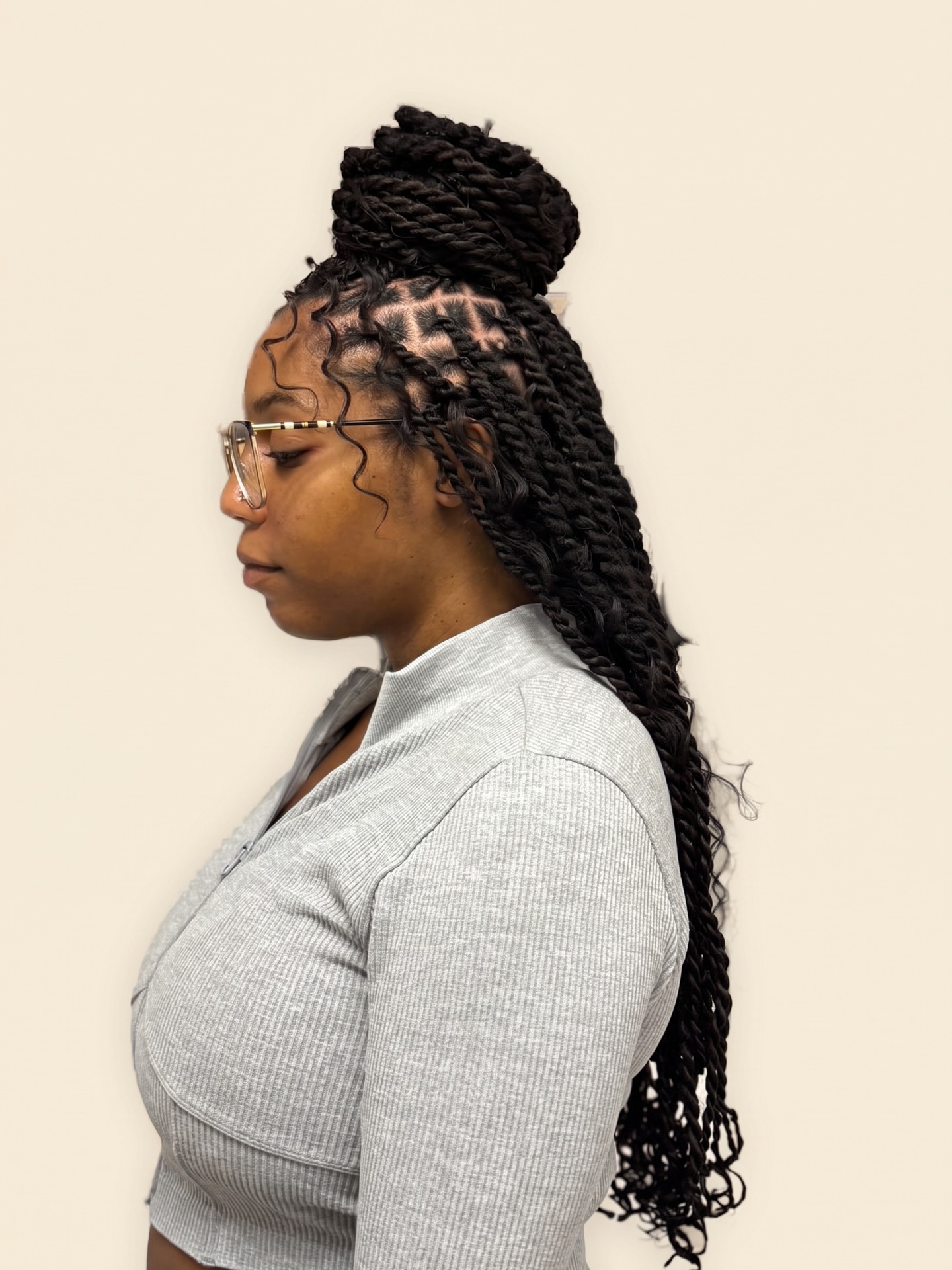 Client shown from the side with long black twists gathered in a high bun, on a cream background